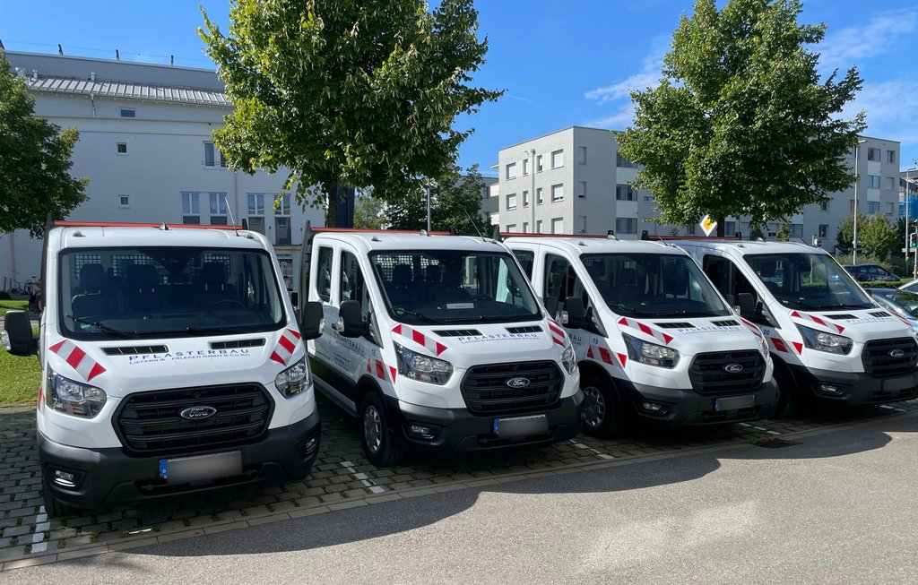 Vier weiße Ford Transit mit einheitlicher Pflasterbau-Beschriftung und rot-weißen Markierungen