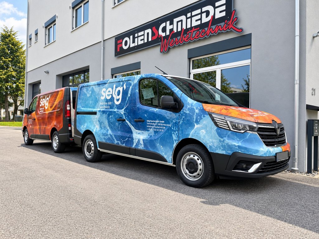Blau und orange gestaltete Transporter von Selg Haustechnik vor der Folienschmiede – blauer Transporter im Vordergrund